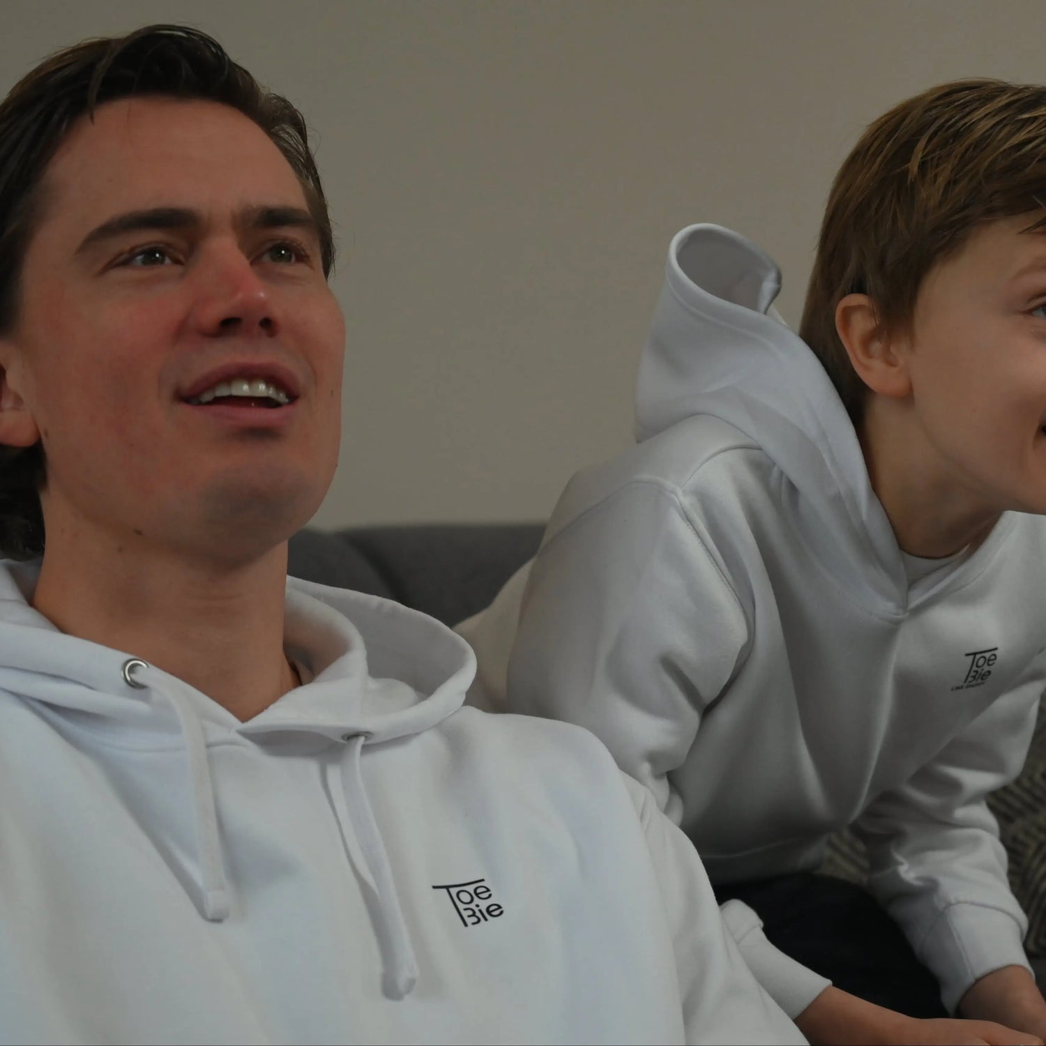 vader en zoon dragen dezelfde hoodie, terwijl ze aan het gamen zijn op de bank