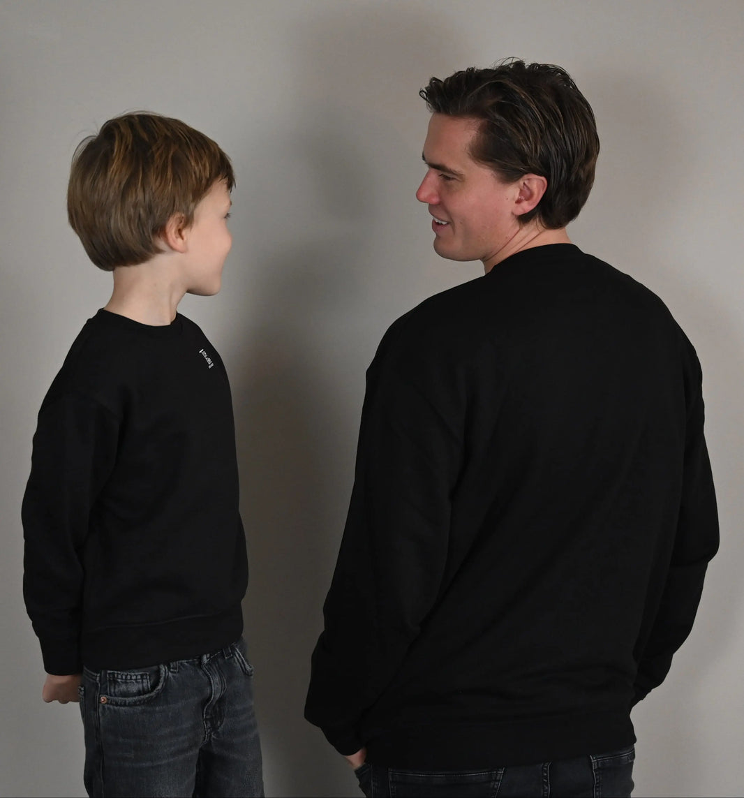 vader en zoon dragen dezelfde toebie sweater in het zwart terwijl ze elkaar aankijken en lachen