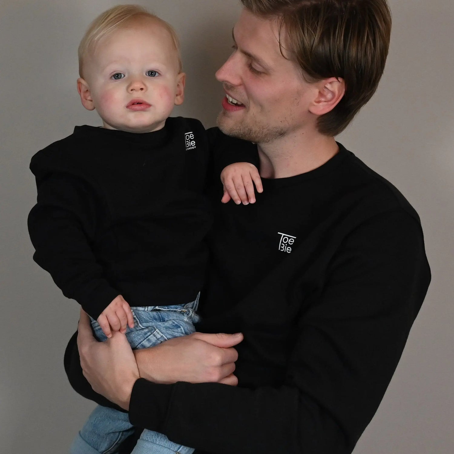 vader houdt zijn zoon vast voor de foto, terwijl ze dezelfde sweater dragen