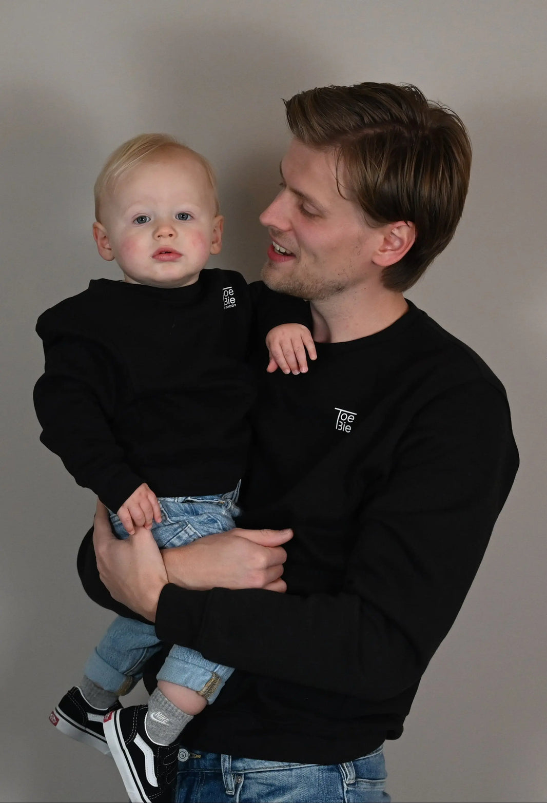 vader houdt zijn zoon vast voor de foto, terwijl ze dezelfde sweater dragen