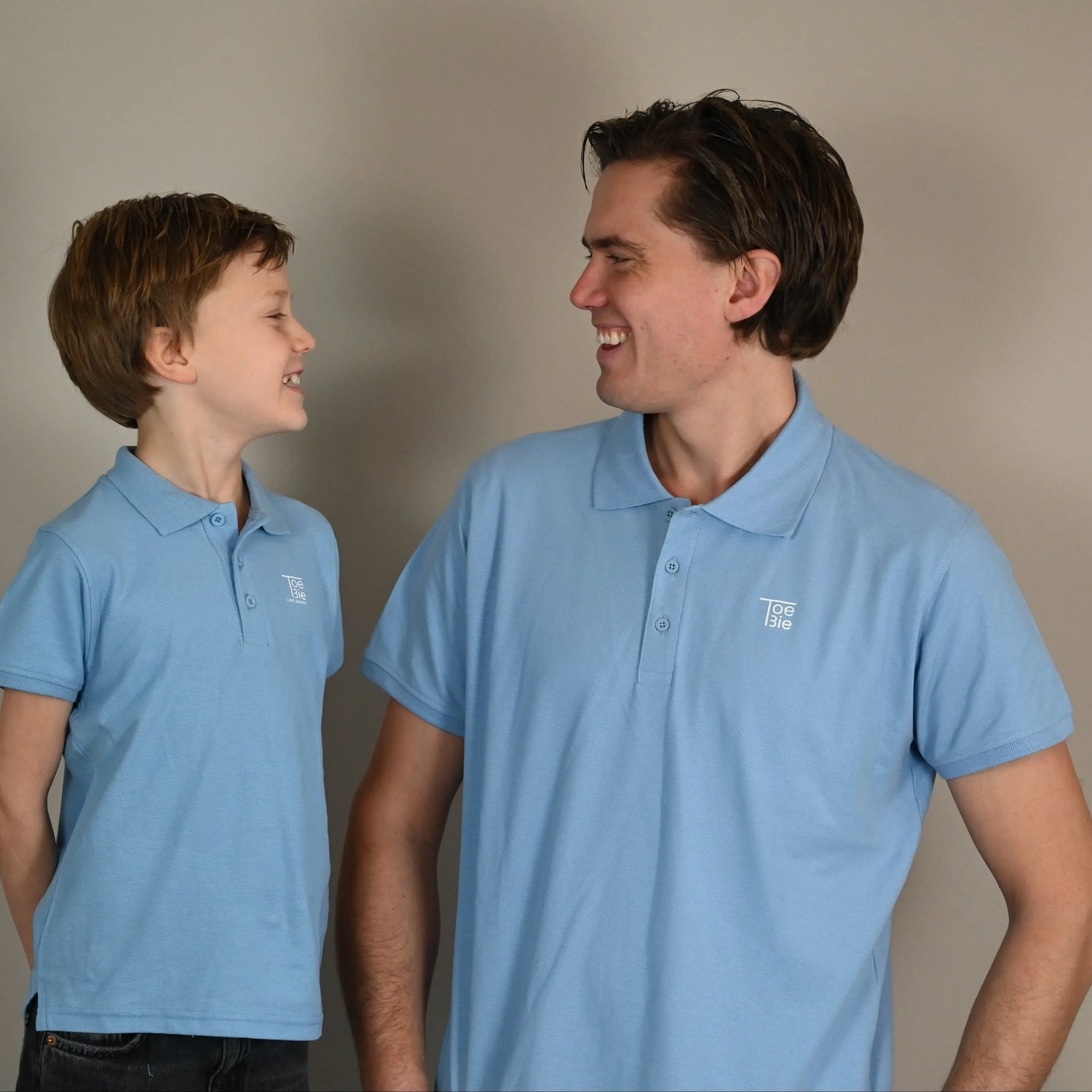 Vader en zoon kijken elkaar lachend aan, terwijl ze dezelfde polo dragen