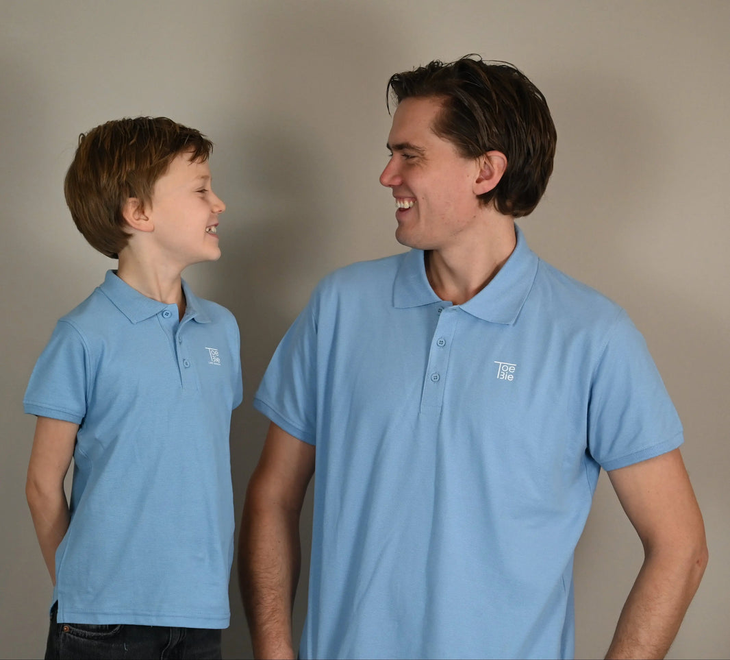 Vader en zoon kijken elkaar lachend aan, terwijl ze dezelfde polo dragen