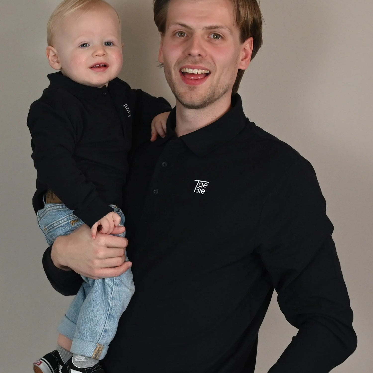 Vader en zoon dragen dezelfde polo met lange mouw en kijken lachend in de camera
