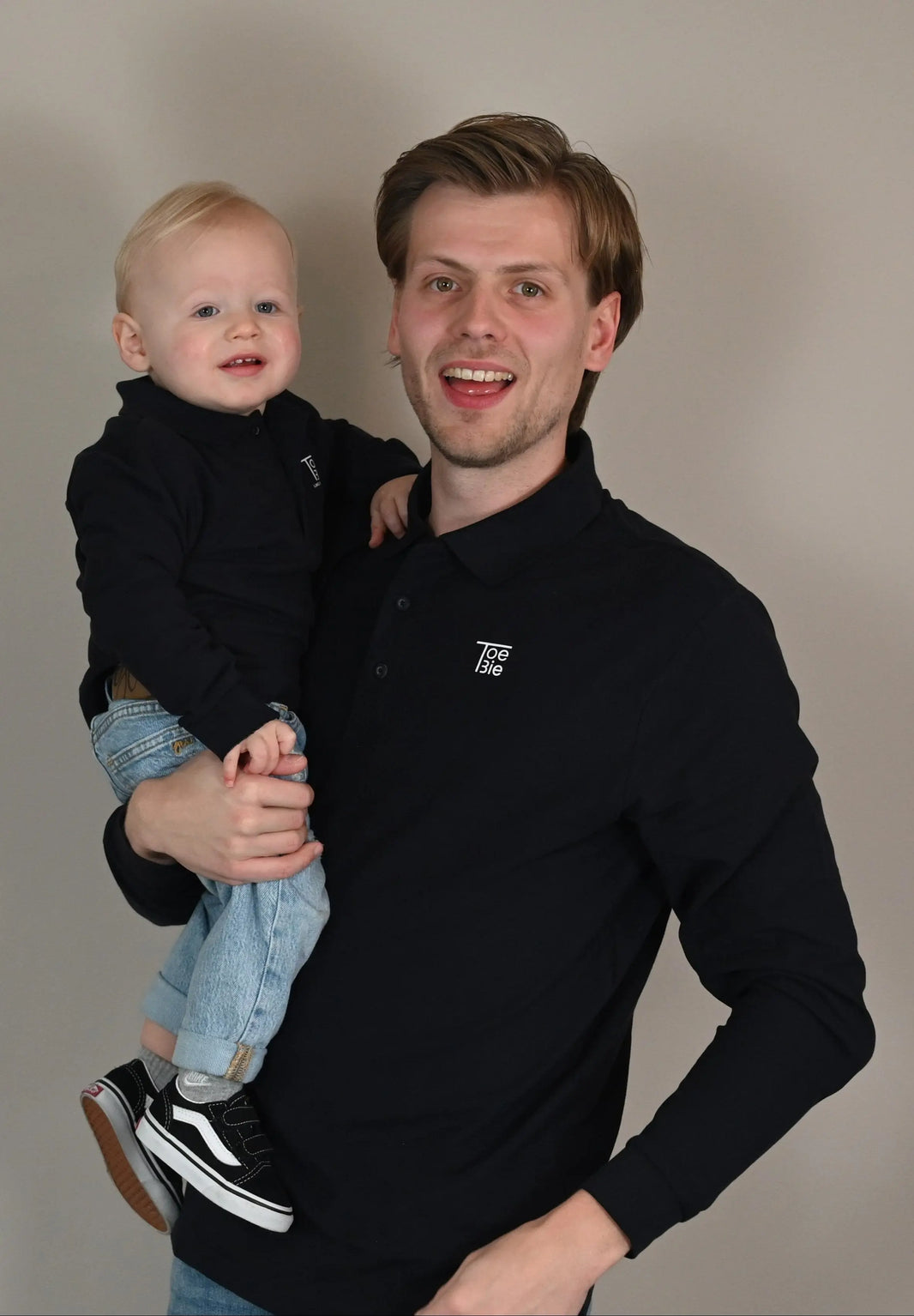 Vader en zoon dragen dezelfde polo met lange mouw en kijken lachend in de camera