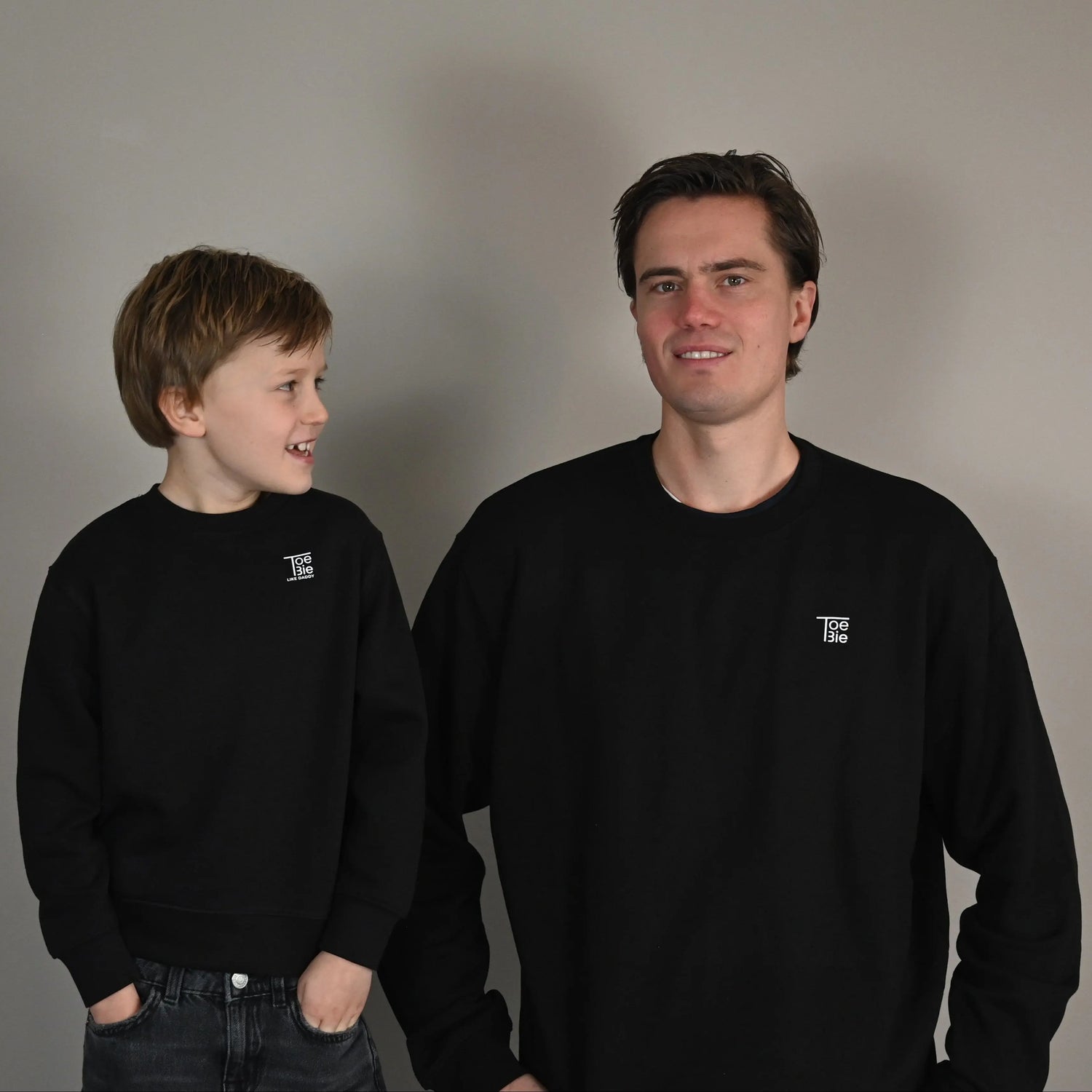 vader en zoon dragen dezelfde sweater in het zwart, terwijl ze met hun handen in hun zakken staan te lachen