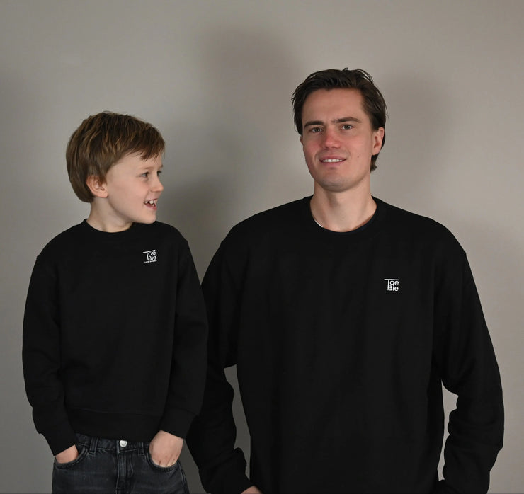 vader en zoon dragen dezelfde sweater in het zwart, terwijl ze met hun handen in hun zakken staan te lachen