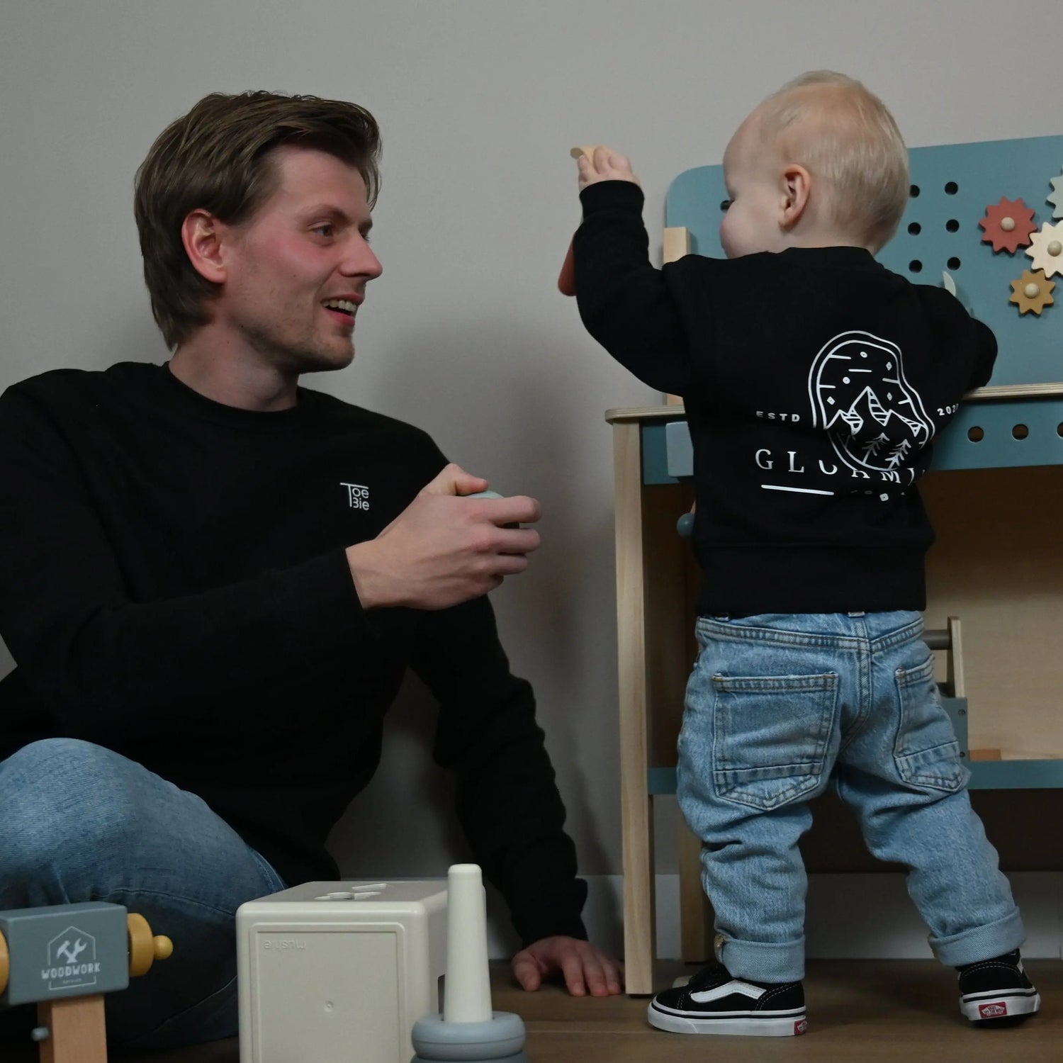 Vader en zoon zijn aan het spelen met een mini werkbank terwijl ze dezelfde sweater dragen